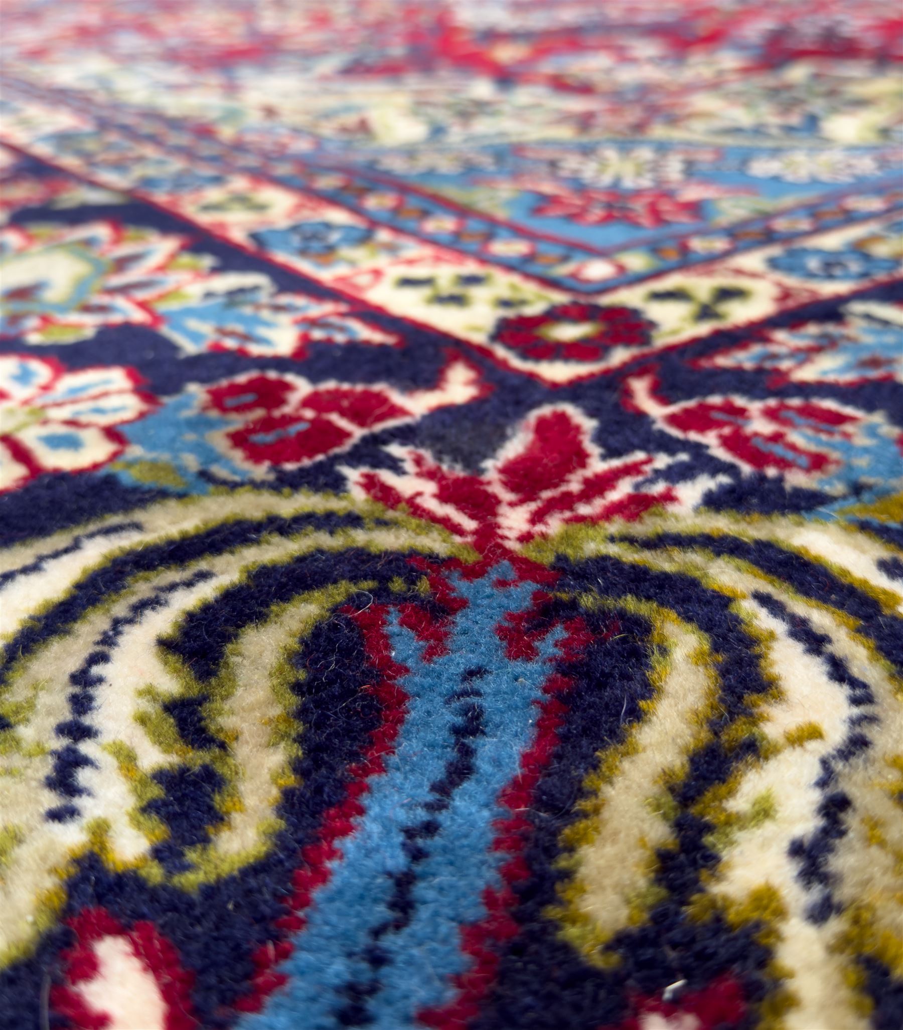 Central Persian Isfahan Carpet, hand-knotted, featuring a bold central rosette medallion on a rich red field, flanked by stylised floral sprays, scrolling foliage and mythical animals, within a broad indigo border decorated with alternating cartouches and flowerheads