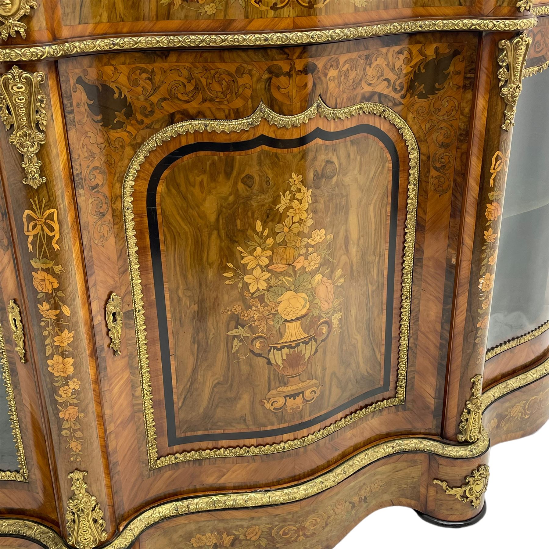 Victorian design inlaid figured walnut credenza sideboard, shaped form with crossbanded and book-matched top, the frieze rails inlaid with foliage scrolls and flower heads, central panelled door inlaid with floral urn flanked by two glazed doors, on shaped plinth base inlaid with foliate decoration, mounted by cast gilt metal masks and floral egg and dart beading 