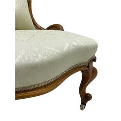 Victorian walnut framed nursing chair, the cresting rail decorated with carved applied flower heads and acanthus leaves, shaped back and sprung seat upholstered in buttoned ivory damask fabric, serpentine front over cartouche carved cabriole supports with ceramic castors (W57cm H92cm); with matched footstool, circular top over shaped moulded apron, on floral carved cabriole feet (W34cm) 