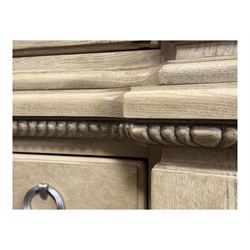 Brunswick - washed oak finish illuminated display cabinet, upper section with four glass-panelled doors enclosing glass shelving, base fitted with two drawers over four paneled cupboard doors, each fitted with distinctive round metal handles, raised on plinth base