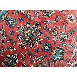 Persian Kashan red ground rug, the field decorated with trailing leafy branches and large palmettes, scrolling border decorated with stylised plant motifs and flower heads, within guard stripes