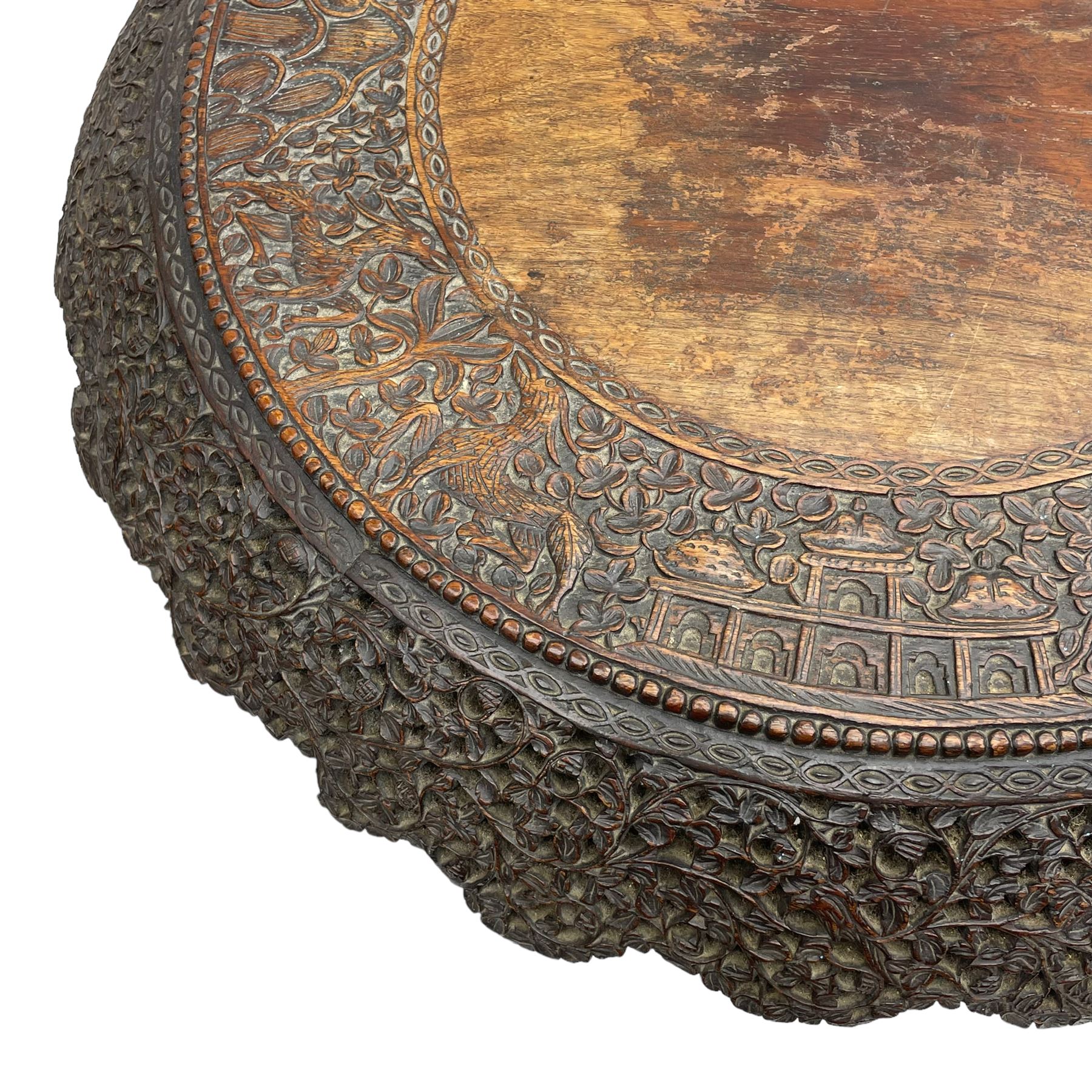Late 19th century Anglo-Indian carved hardwood occasional table, circular tilt-top carved profusely with mythical animals and foliage decoration, pierced and carved with interlaced leafy branches, leaf carved pedestal supports on a raised platform with further carved and pierced foliage decoration, four carved feet in the form of mythical beasts with gaping jaws 