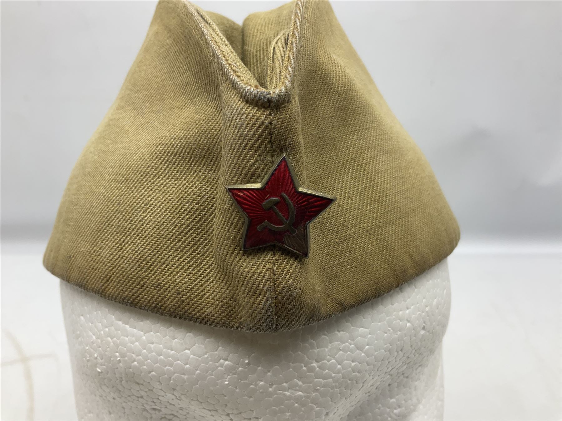 Four side caps - WW2 Russian, post-WW2 Russian and two East German; all with badges, one with multiple metal badges (4)