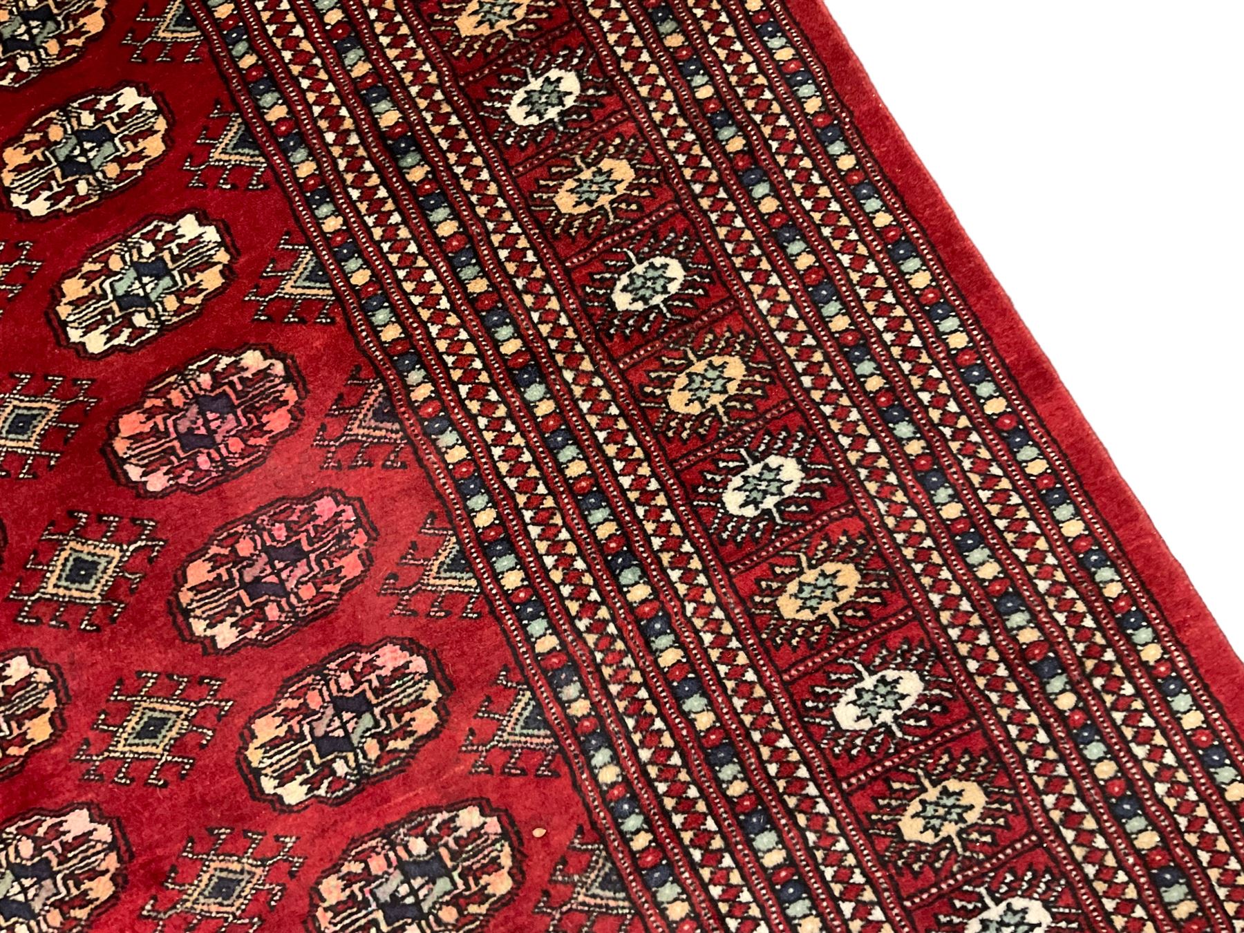 Pakistani Bokhara red ground rug, the field decorated with repeating Gul motifs and lozenges, the multi-band border with stylised plant motifs with dark indigo outlines