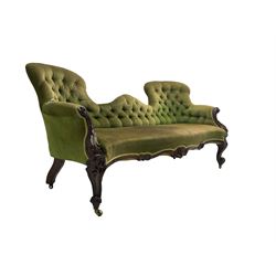 Victorian rosewood framed serpentine settee, upholstered in buttoned laurel green fabric with sprung seat, scrolled arms with carved foliate decoration, apron carved with central cartouche, raised on cabriole supports with brass castors