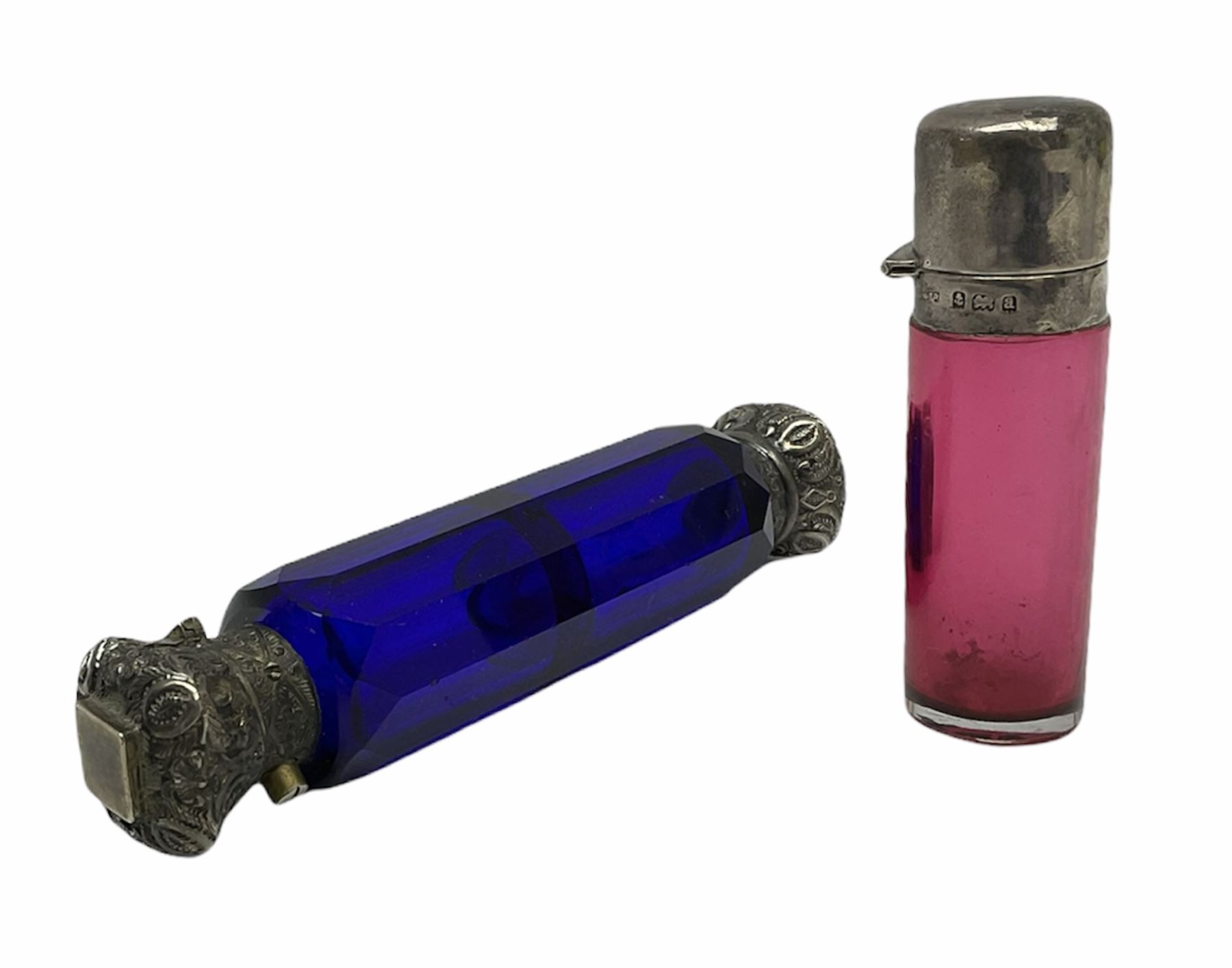 Late Victorian silver mounted ruby glass cylindrical scent bottle, with interior glass stopper, Birmingham 1900, makers mark worn, H8cm, together with a Victorian double ended cut blue glass perfume bottle mounted with white metal screw and flip caps decorated with foliate repousse detailing, H13.5cm