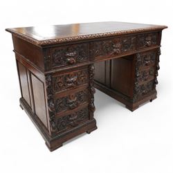 Victorian carved oak twin pedestal desk, moulded and foliate carved rectangular top with leather inset, fitted with nine drawers, each carved with scrolling foliage and lion mask handles, on skirted base 