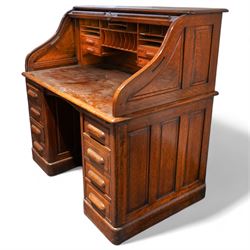 Early 20th century oak twin pedestal roll top desk, tambour roll enclosing small drawers and pigeon holes, fitted with seven drawers, on plinth base 