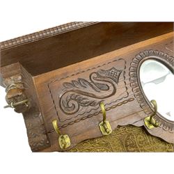 Late 20th century oak wall hanging coat rack, central bevelled oval mirror in foliate carved surround, decorated with S-scrolls and lion masks, fitted with needlework hanging 