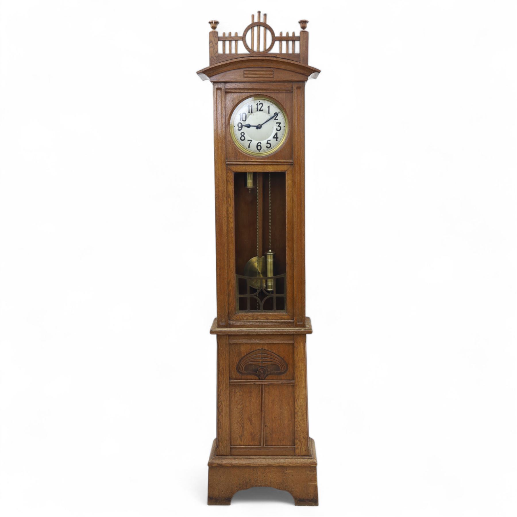 German-Art Deco 8-day longcase clock in an oak case, with a curved top and open fence work pediment, with reeded decoration and a fully glazed case door with a rectangular brass open work panel, on a tall rectangular plinth with a period  carved motif, circular slivered dial with Arabic numerals and spade hands, two train HAC (Hamburg and American Clock Company) weight driven movement, sounding the hours and half-hours on a coiled gong, with weights and pendulum.   