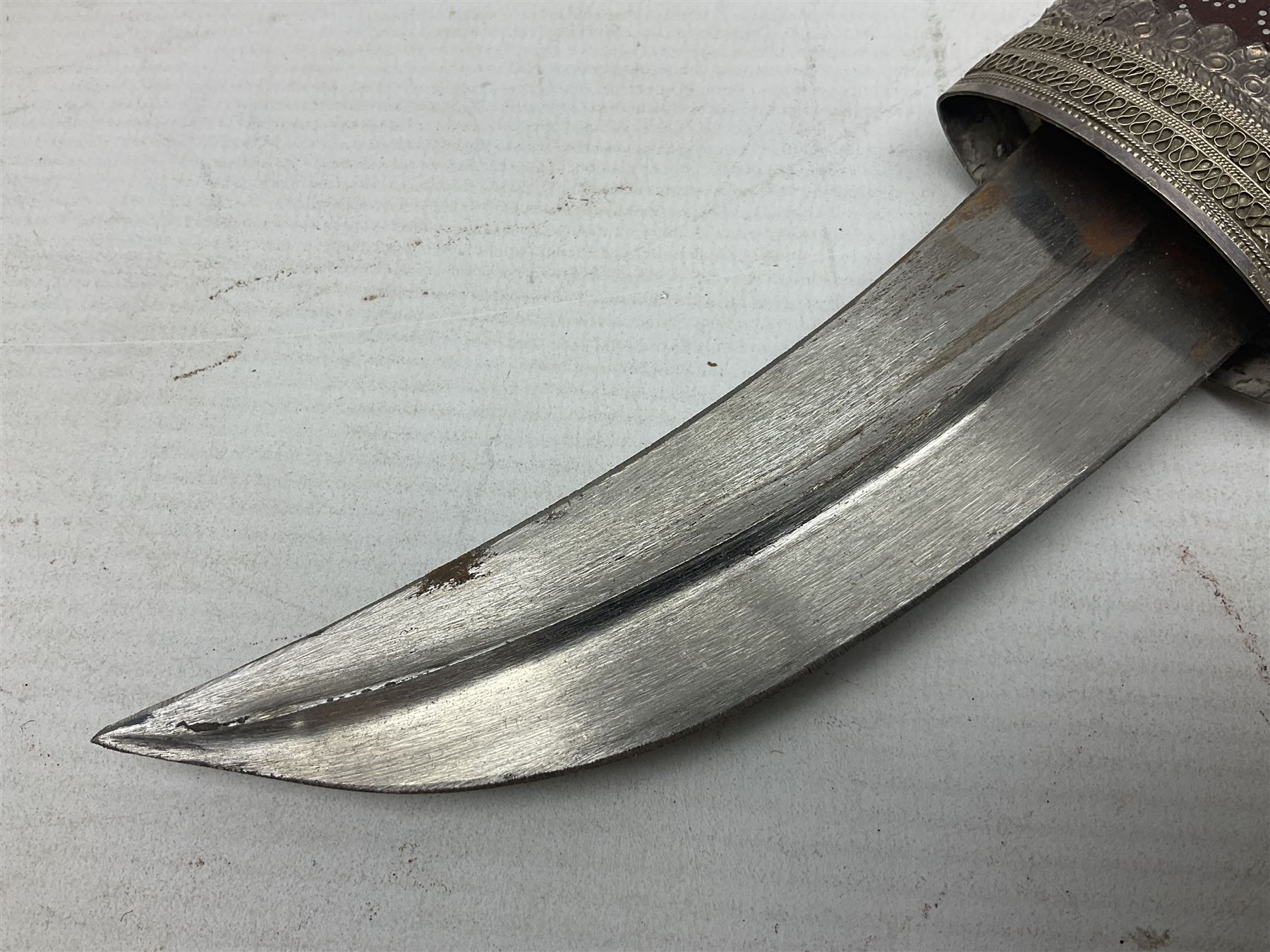 Omani Khanjar dagger, the 12.5cm curved blade with pronounced medial rib to either side, waisted horn style hilt with dome shaped pommel and inlaid pique work; in an intricately filigree decorated white metal scabbard with rings woven into the belt mount L25cm overall