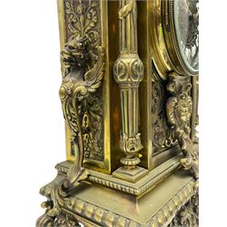 French - Late 19th century brass cased 8-day mantle clock, with a break arch top surmounted by a reeded urn with handles, brake front case with finials and recessed reeded columns on a stepped plinth raised on scroll feet,  brass dial with cartouche roman numerals and brass hands within a glazed dial bezel, twin train rack striking movement, striking the hours and half-hours on a bell. With pendulum. 