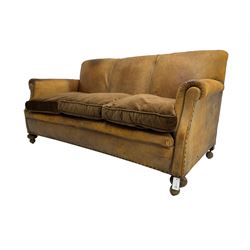Early-to-mid-20th century three seat sofa, upholstered in worn tan leather with studwork, loose cushions upholstered in brown fabric, on compressed bun feet with castors