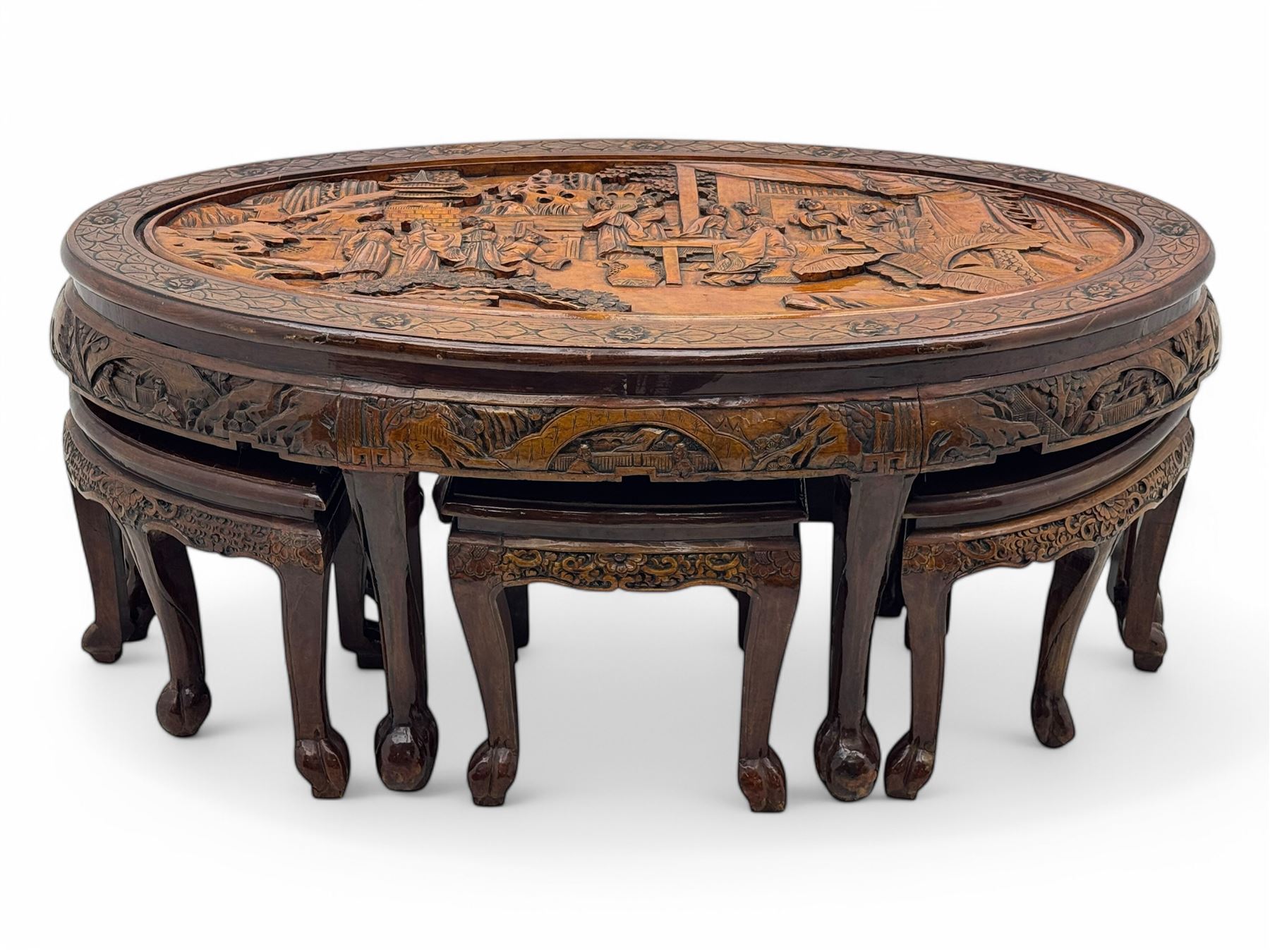 Early 20th century Chinese hardwood nesting coffee table, oval top carved with figures and traditional pagoda scenes with carved frieze, complete with six inset stools or side tables, raised on tapering supports with paw feet