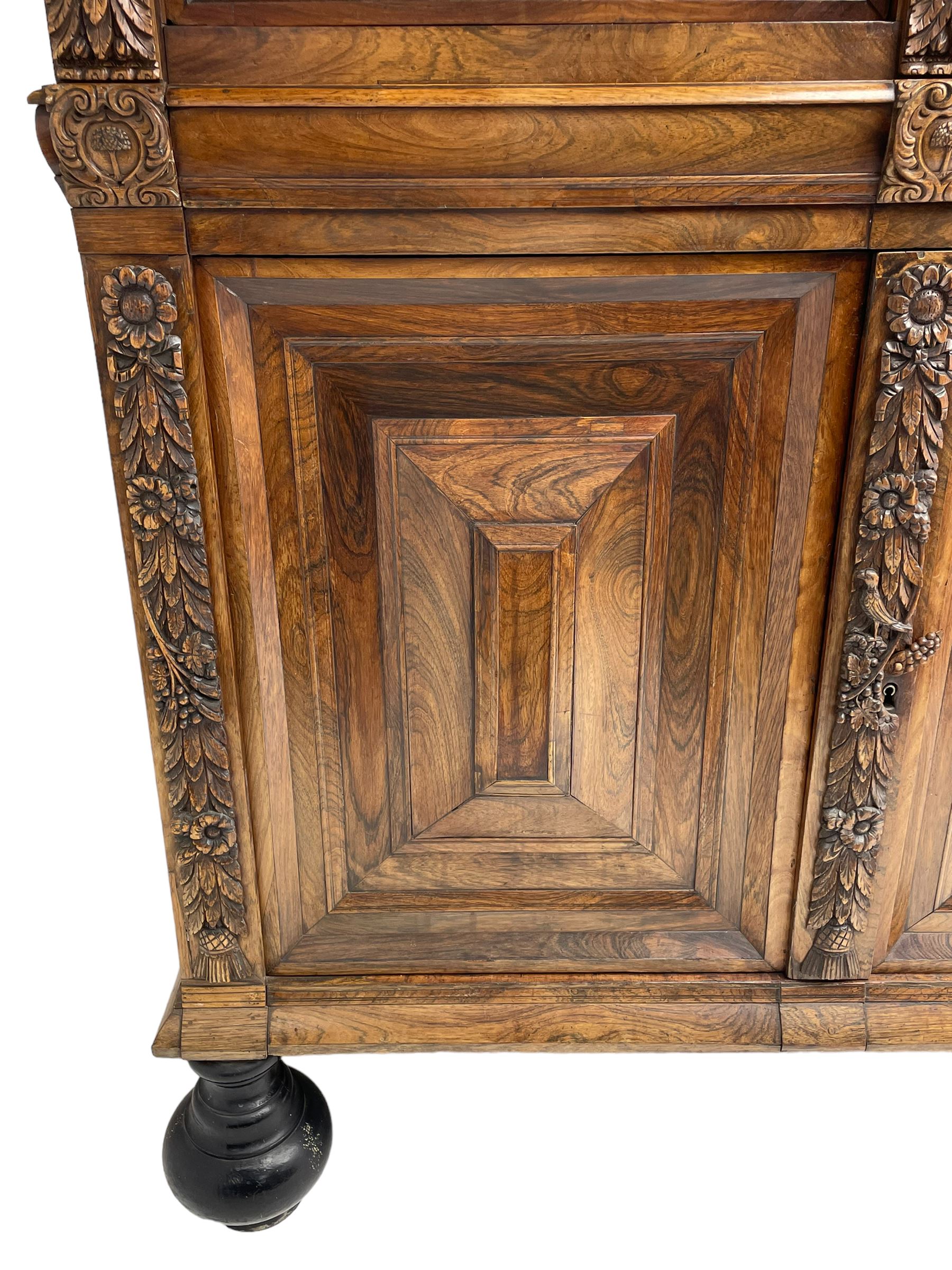 Late 17th century Flemish/Dutch rosewood and oak ‘Zeeuwse Kast’ or cupboard, projecting cornice carved with three putti masks, the uprights carved with lion masks over ribbons, flower heads and foliage, enclosed by four geometric panelled doors, lower central upright carved with flower head over foliate ribbon with bird among foliage, the escutcheon hidden by swivel berry carved cover, interior fitted with shelves, two drawers and shallow hinged cupboard, on two large turned and ebonised feet, circa 1680
