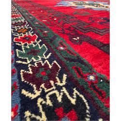 Northwestern Persian Cirjan hand-knotted carpet, madder red field with three linked stepped lozenge medallions in blue, ivory and green, flanked by angular motifs within a dark green border of serrated leaves and rosettes 