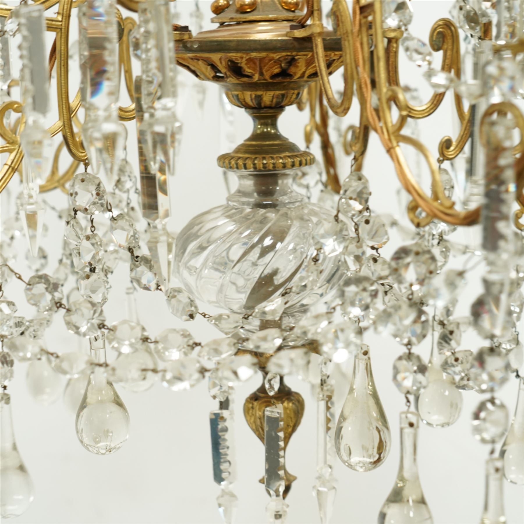 Late Victorian gilt bronze mounted crystal chandelier, ceiling rose above shaped top of trailing swags, glass crystal droplets, beneath rising curled branches and glass beads tapering down to five candle sconces, inside circular bezel fitted with drops and glass twist fluted stem, supported with an internal metal shaft above a rococo style stem holding double branches, and similar styled branches, with twelve branches fitted with candle holders and drip trays with crystal drops and cut crystal spears, the underside festooned with crystal glass swags and a bulbous fluted glass terminal and shaped finial with crystal glass swags attached to the branches, the base with pear shaped droplet graduating to the centre, wired for electricity 