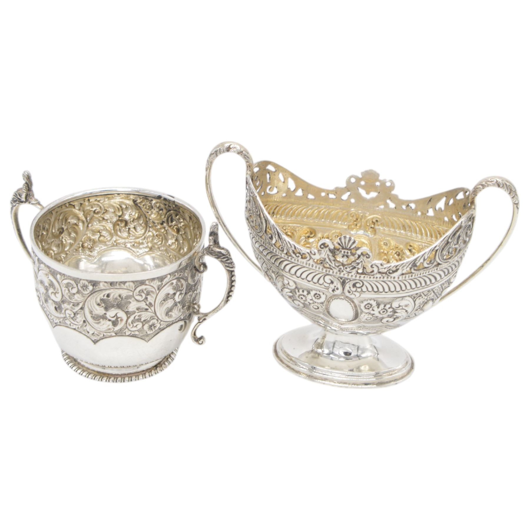 Late Victorian silver twin handled sugar bowl, profusely embossed with floral and scrolling decoration and acanthus capped handles, upon stepped oval base, hallmarked Josiah Williams & Co, London 1897, together with a Victorian twin handled sugar bowl, of circular form with embossed and chased foliate decoration and seated figures capping each handle, upon circular base, hallmarked London 1888, maker's mark indistinct, tallest H11cm