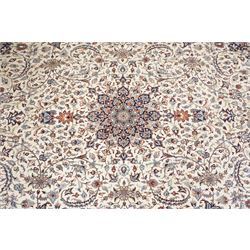 Persian ivory ground Kashan carpet, the busy field decorated with a central floral pole medallion with matching spandrels, the field profusely decorated with scrolling foliate motifs, the crimson guard stripe with repeating scrolling palmettes