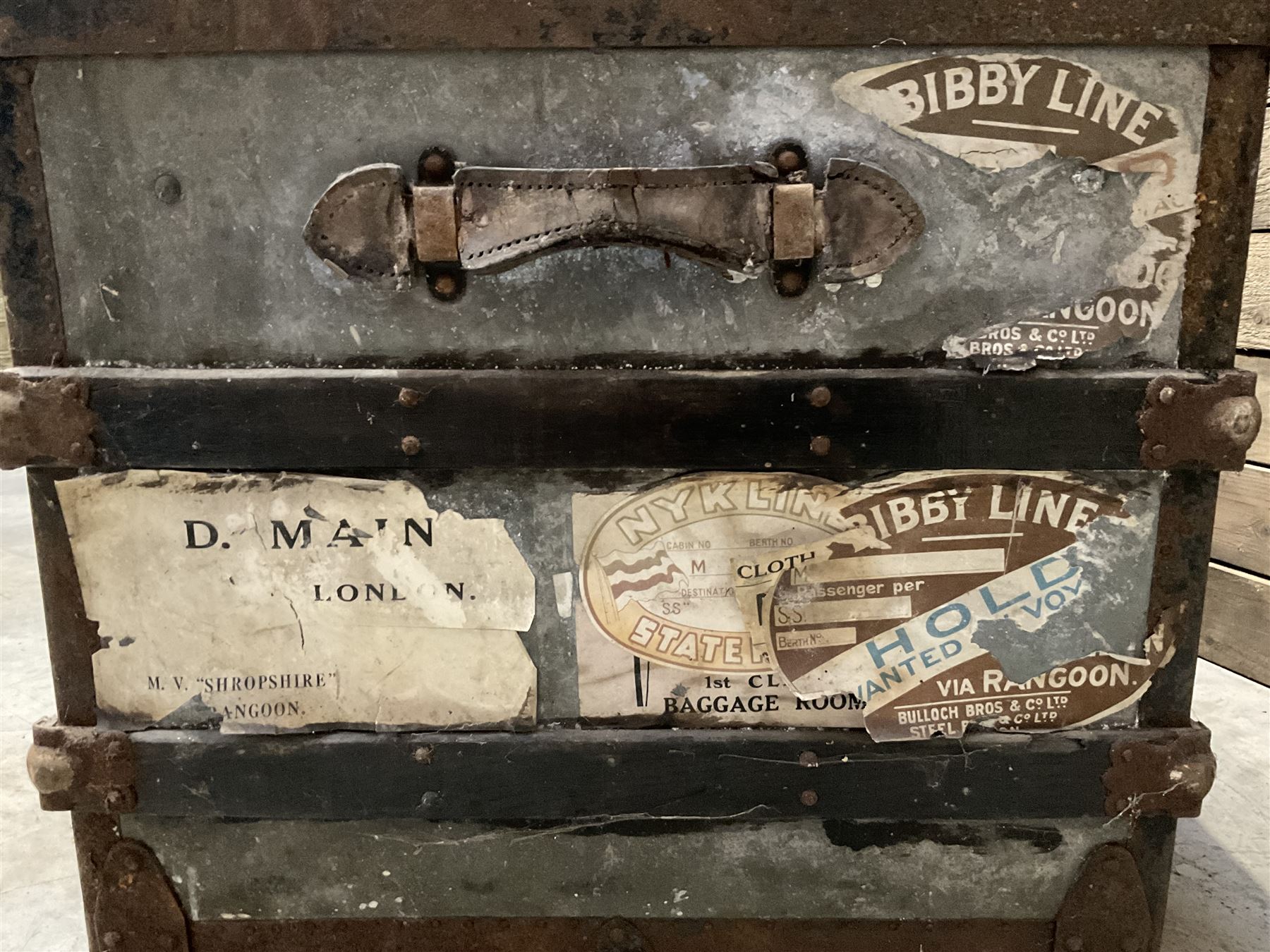 Early 20th century wood and metal bound zinc travelling trunk, hinged top with three clasps, decorated with period luggage labels