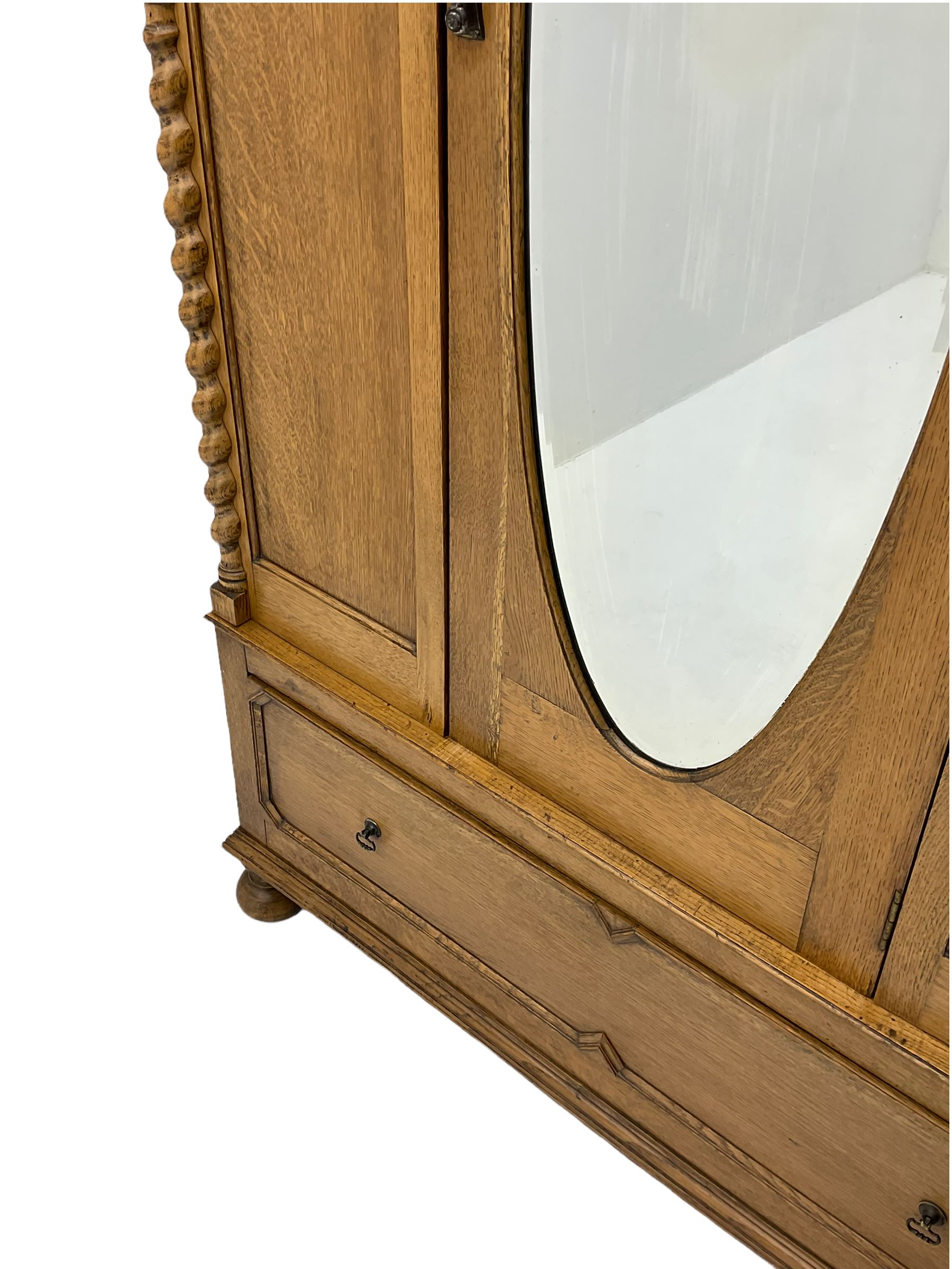 Early 20th century oak wardrobe, projecting cornice of blind fret-work frieze, oval bevel edge mirror door, half spiral turned pilasters, drawer to base with mouldings, on turned bun feet