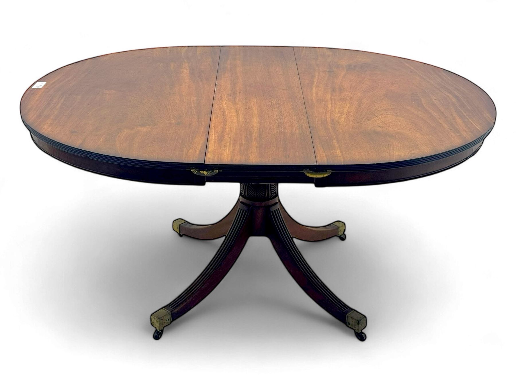 Regency design mahogany extending dining table, circular top with reeded edge and pull-out mechanism to accommodate additional leaf, raised on a carved central baluster column with acanthus detailing, supported by a quadruple reeded splay base terminating in brass caps and castors

