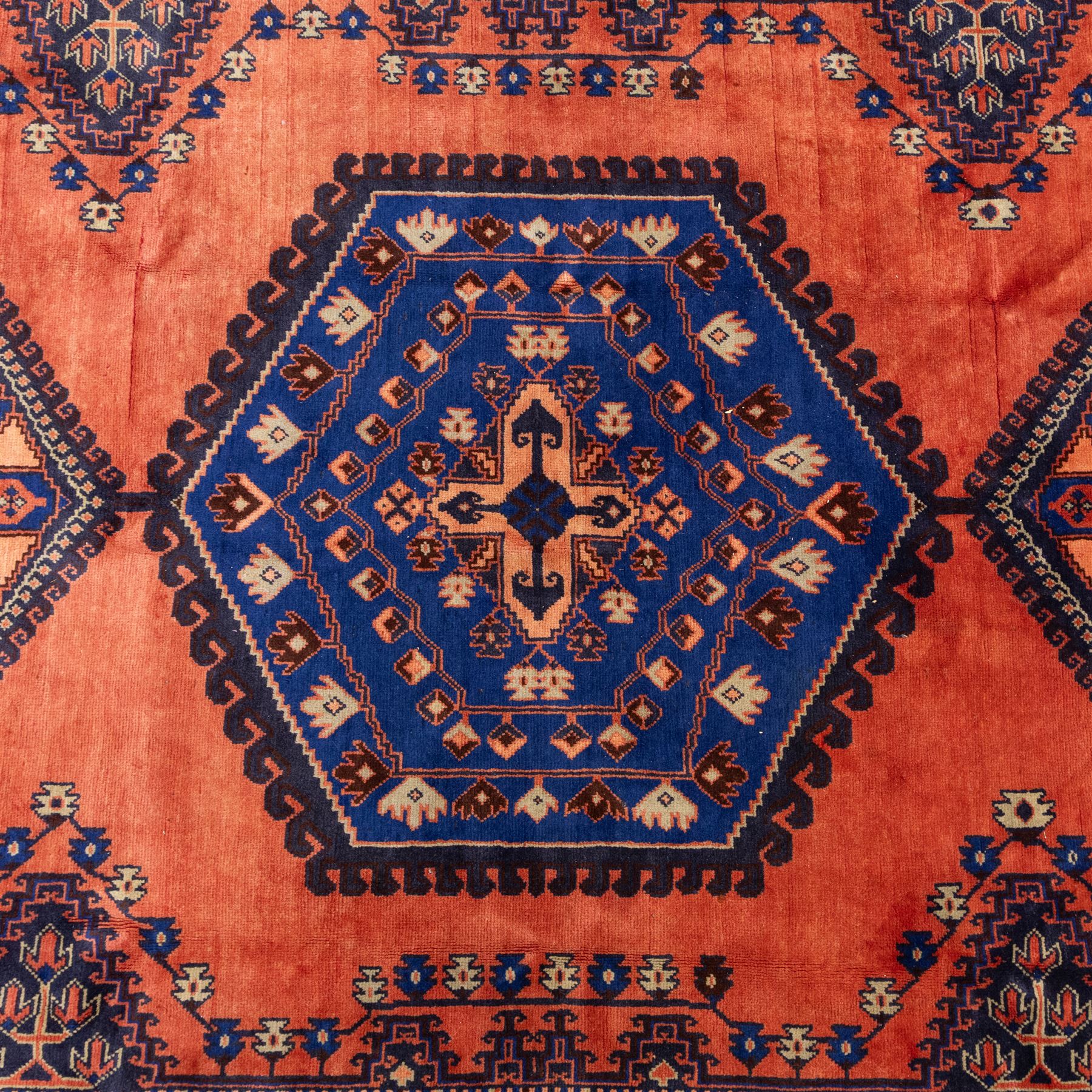 Central Persian Veis hand-knotted carpet, madder red field, decorated with a repeating arrangement of large octagonal and diamond medallions filled with stylized cross and geometric motifs and angular tribal devices within a series of geometric borders in tones of madder red, indigo blue, ivory, and soft green, with cotton fringe ends 
