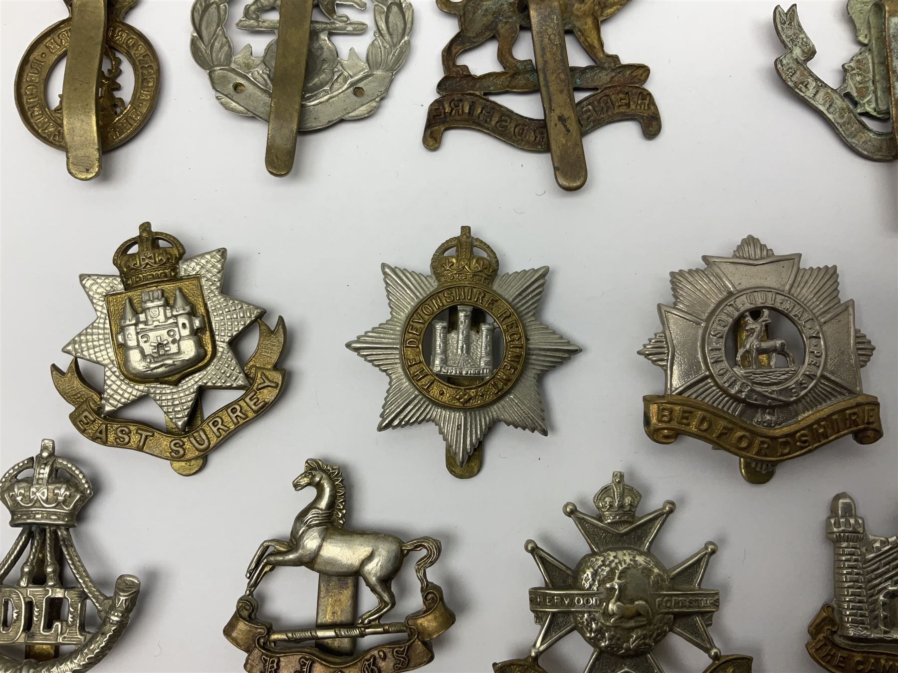 Twenty cap badges including Hertfordshire, Royal Sussex, Cambridgeshire, Hampshire, Notts and Derby, East Surrey, Herefordshire, South Lancashire, Devonshire, Bedfordshire, Durham Light Infantry etc (20)