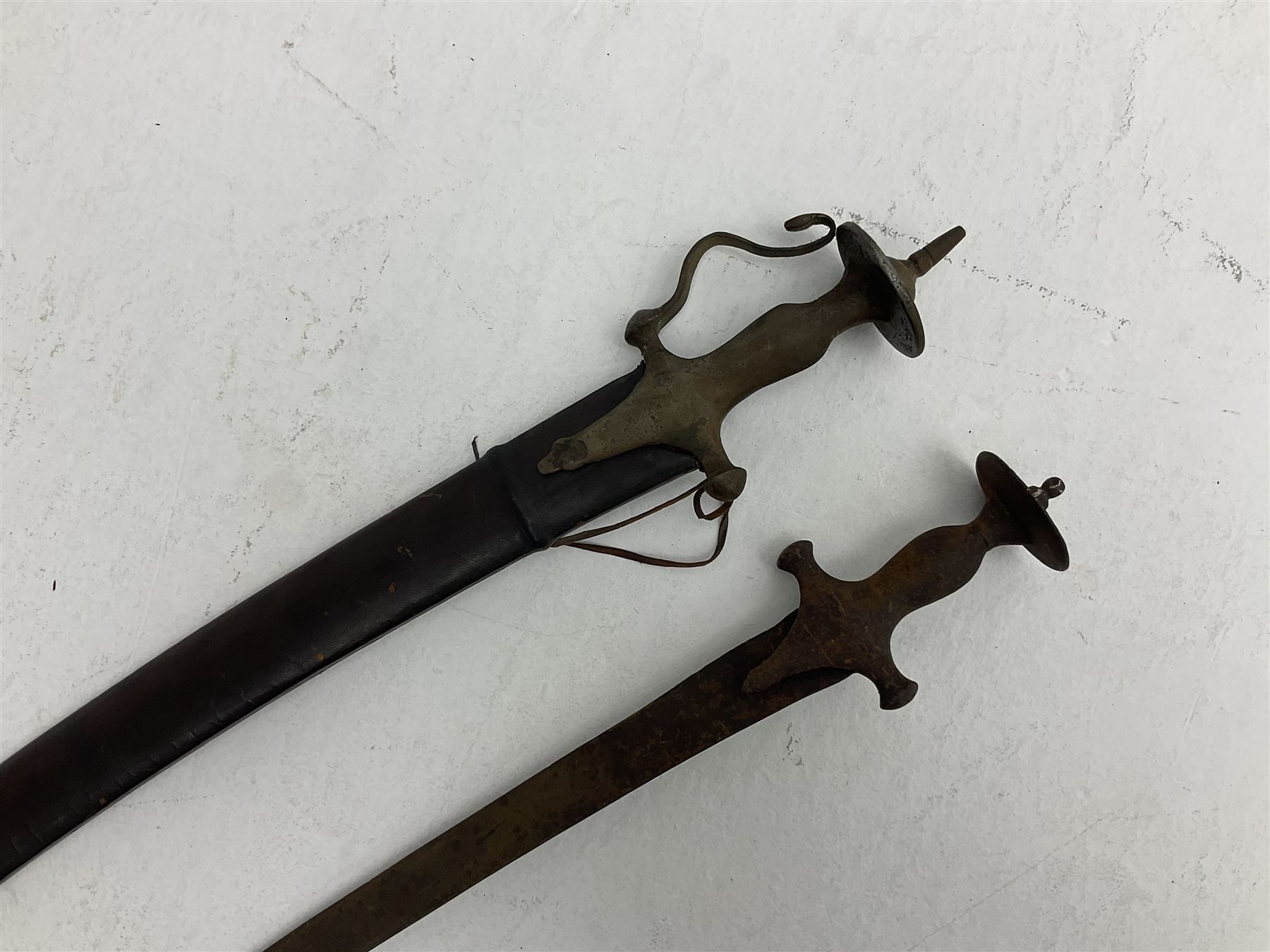 Late 19th/early 20th century Indian Tulwar sword with 81cm plain curving steel blade and iron hilt with extended langets, knucklebow and spiked pommel; in leather covered scabbard L100cm overall; and another Tulwar lacking scabbard in almost relic condition (2)