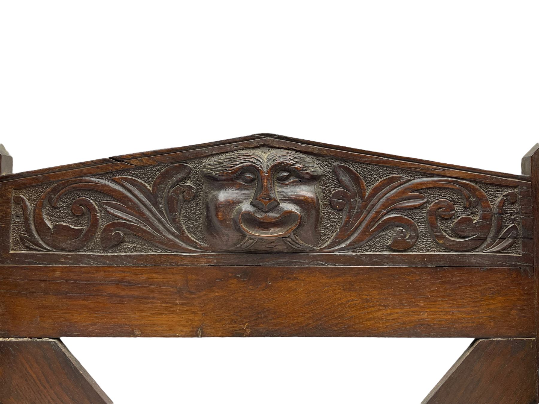 Victorian oak wall hanging whip or stick rack, sloped arch pediment carved with central grotesque mask with extended scrolling foliage, the upright supports cut with rests, x-framed back, two lower hooks