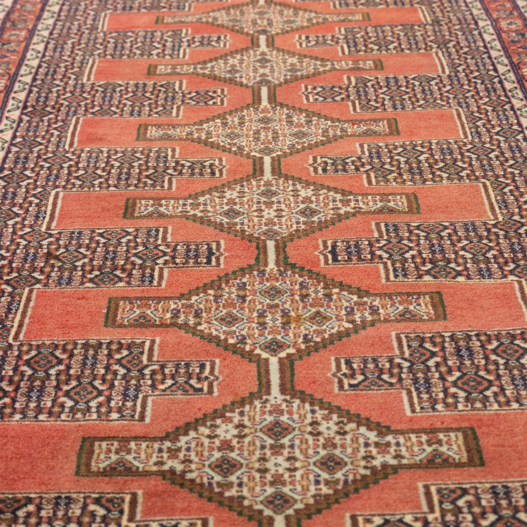 North West Persian Senneh hand-knotted runner, decorated with a continuous series of stepped and hooked geometric medallions against a madder red ground, enclosing herati style and small geometric floral motifs, framed by a principal border and flanked by multiple narrow guard stripes, with cotton fringe ends 
