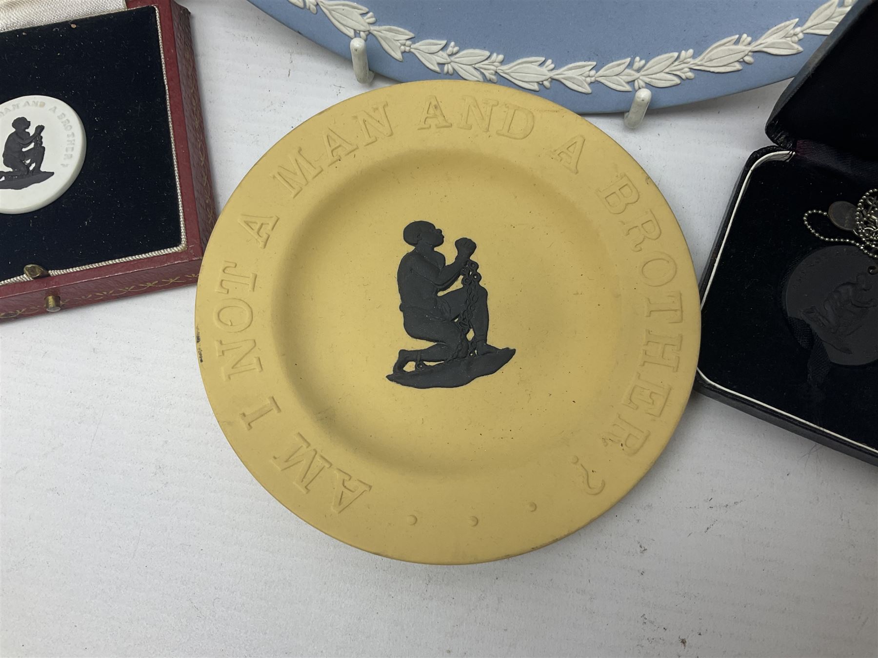 Group of William Wilberforce Abolition of Slavery items, comprising Wedgwood black on cane Jasperware pin tray, Wedgwood light blue Jasperware plate, and two Wedgwood oval medallion pendants, each depicting a kneeling figure beneath the inscription 'AM I NOT A MAN AND A BROTHER?', an Eastgate pottery plaque decorated in relief with a kneeling figure before William Wilberforce, a Hull Museum Publications pamphlet titled 'Medals, Tokens, etc., Issued in Connection with William Wilberforce and the Abolition of Slavery', by Thomas Sheppard, dated 1916, and an antique print depicting William Wilberforce after the original portrait by George Richmond, (7)
