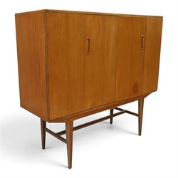 Alfred Cox - mid-20th century teak cabinet, rectangular top over two bifold doors with inset handles, opening to reveal three central graduating drawers surrounded by assorted shelves, raised on tapering supports united by H-stretcher, stamped to inside of drawer