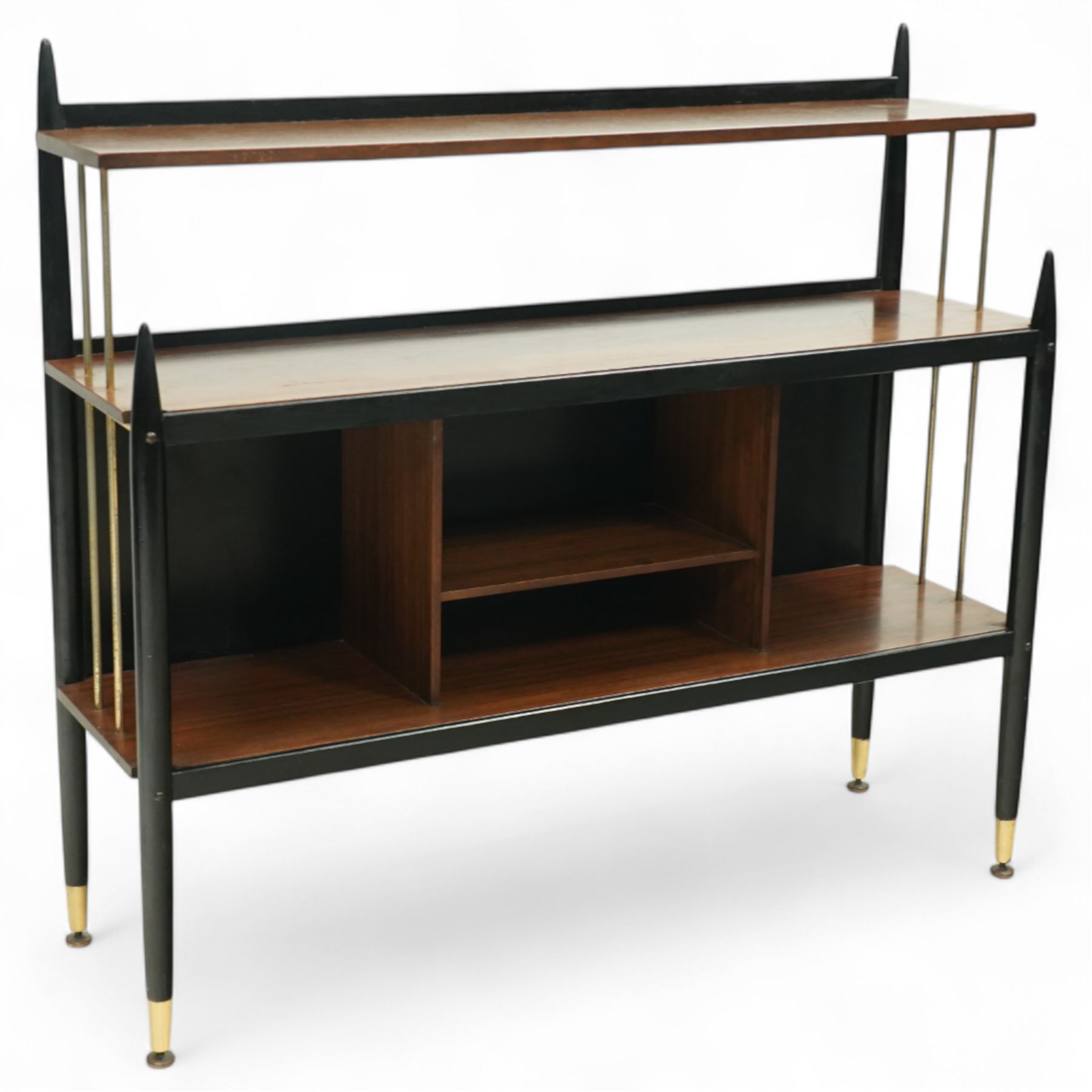 E Gomme for G Plan - 'Librenza' mid-20th century teak and ebonized wood bookcase, rectangular three-tier open shelf design with finials, narrow and raised top shelf above full span and depth central shelf, above divided shelf with open pigeonholes, sides with brass rods, raised on tapering legs with brass capped feet