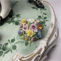 20th century Naples figure group, modelled as a seated female figure playing the lute seated, before a male figure stood holding a sheet of music, each in period dress, upon an oval base with gilt heightened scroll edge, with crowned N mark beneath, H31.5cm L33cm
