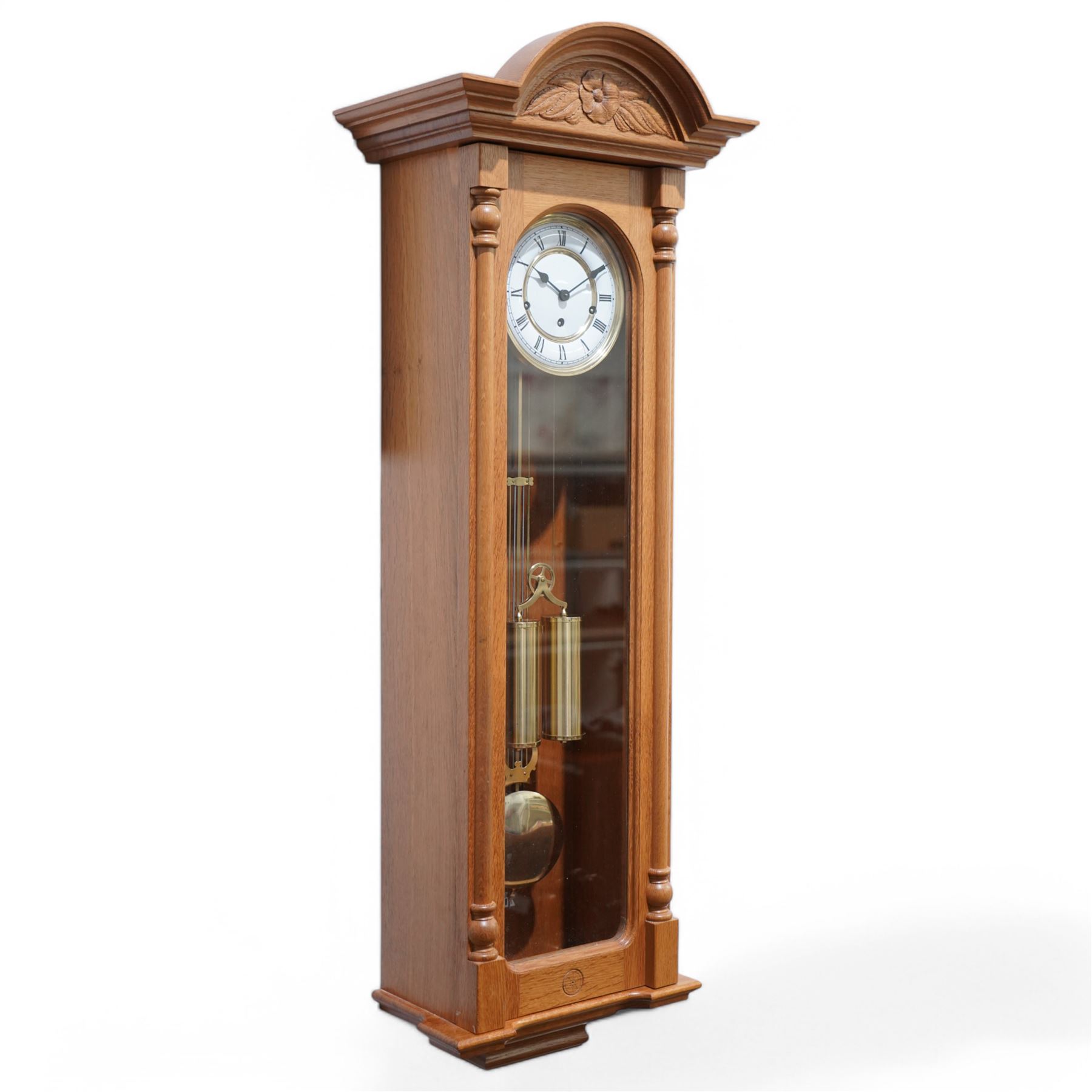 Carthouse - 20th century oak cased 8-day wall clock with a break arch pediment and carved tympanum,  fully glazed case door with full length pilasters, visible gridiron pendulum, beat plate and twin brass cased weights suspended on a single bridge pulley, enamel two part dial with Roman numerals, minute track and spade hands, German, Joseph Kieninger RWS three train movement with a weight  driven going train and spring driven strike and chiming trains, chiming the quarters and striking the hours on gong rods. With weights, pendulum and key.  