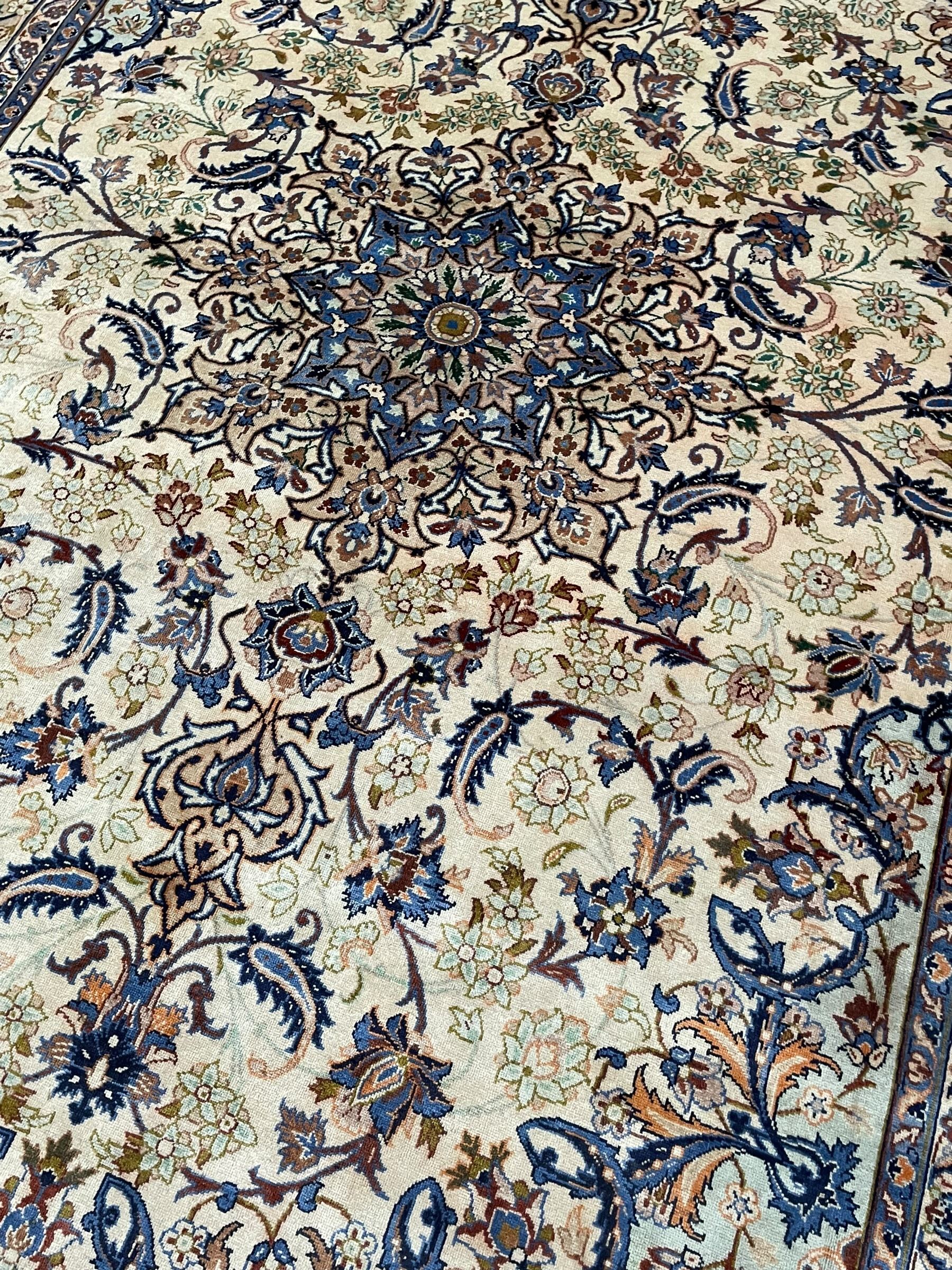 Persian Kashan ivory ground carpet, floral design central medallion surrounded by trailing and interlaced leafy branches with palmettes and flower heads, matching patterned border with guard stripes 