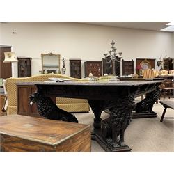 Large 19th century carved oak library table, the rectangular top with lunette carved edge over cartouche panelled and carved  scroll frieze, the central tapering rectangular support relief carved with masks and garlands, on four carved seated lion supports at each corner, on flat angular stretcher with recessed castors stamped ‘Bartholomew & Fletcher, London’