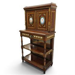 Fine late 19th century Aesthetic Movement ebony and amboyna cabinet on stand with parcel-gilt detail, the moulded cornice with pierced gilt-brass three-quarter gallery above a pair of panelled doors centred by oval porcelain portrait plaques within gilt-metal ribbon-tied frames, the doors further enriched with gilt-metal foliate mounts and flanked by classical figural terms, enclosing a shelved interior, the projecting lower section with amboyna top above a frieze drawer set with a series of floral porcelain roundels within pierced gilt-metal mounts and a central oval floral plaque, raised on turned and fluted supports with gilt-heightened detail, the mirrored back behind two amboyna shelves with pierced gilt-brass galleries, on turned feet