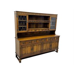 Large mid-20th-century oak dresser with two astragal glazed doors between gallery shelf and lower shelf, with three short drawers and lower section with four drawers and three double-panelled linen-fold hinged cupboard doors 