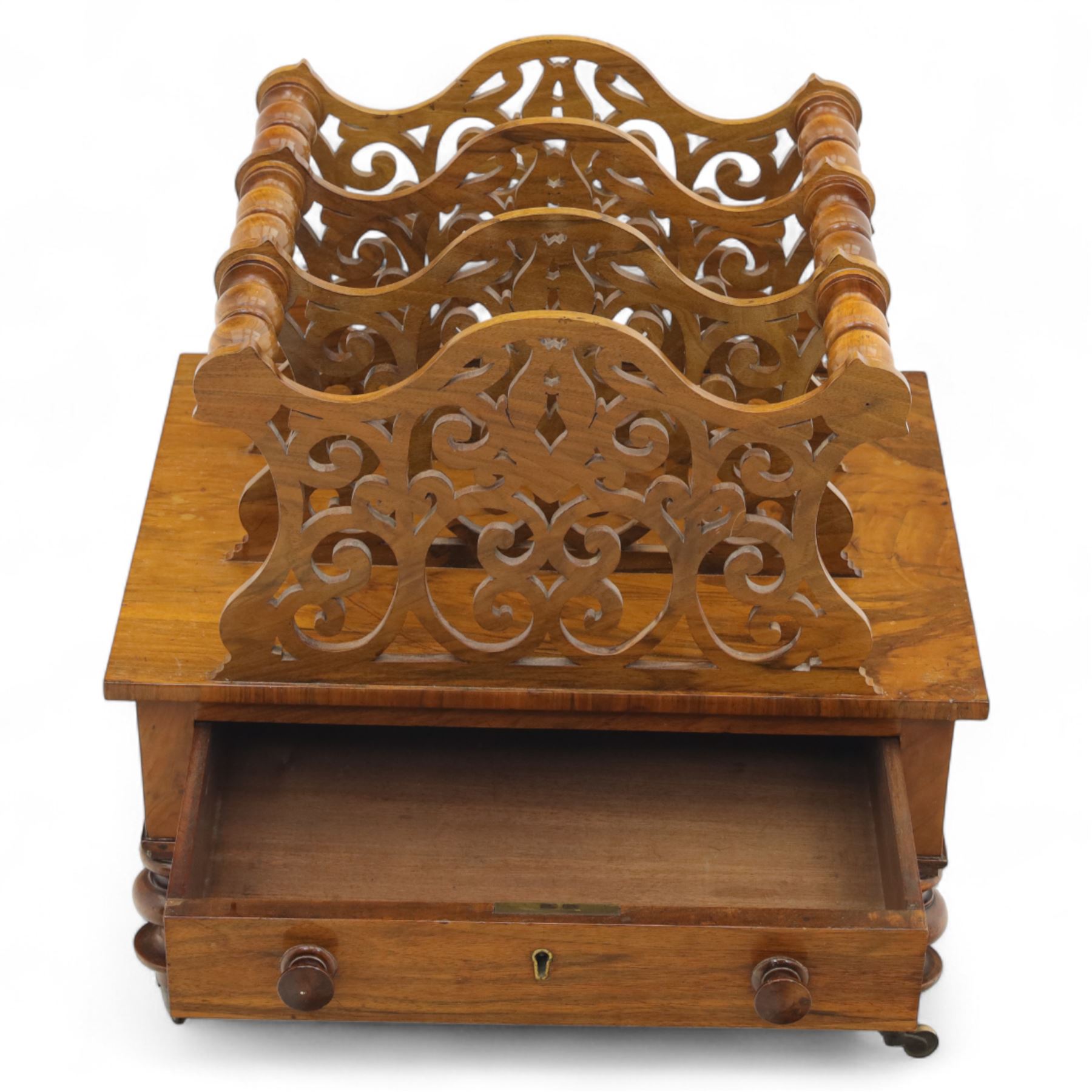 Victorian walnut Canterbury, scroll pierced divisions with turned carrying handles above a frieze drawer with knob handles, raised on turned legs terminating in brass castors