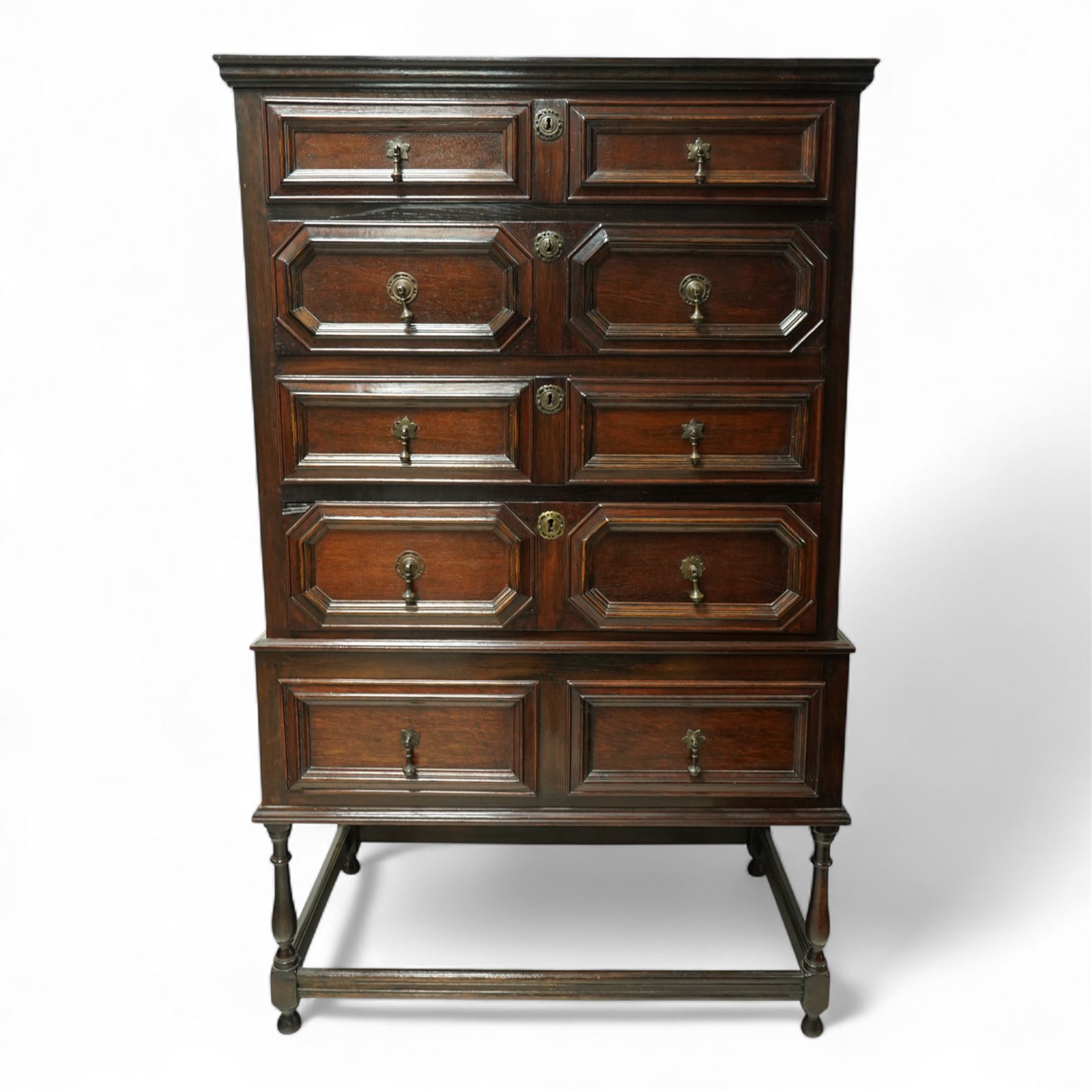 Jacobean style oak chest on stand, four full-length graduated drawers decorated with geometric mouldings, brass pear drop handles and escutcheon, the stand with two drawers above turned legs on a stretcher base on all sides, raised on pear-shaped feet, 18th century and later 

 