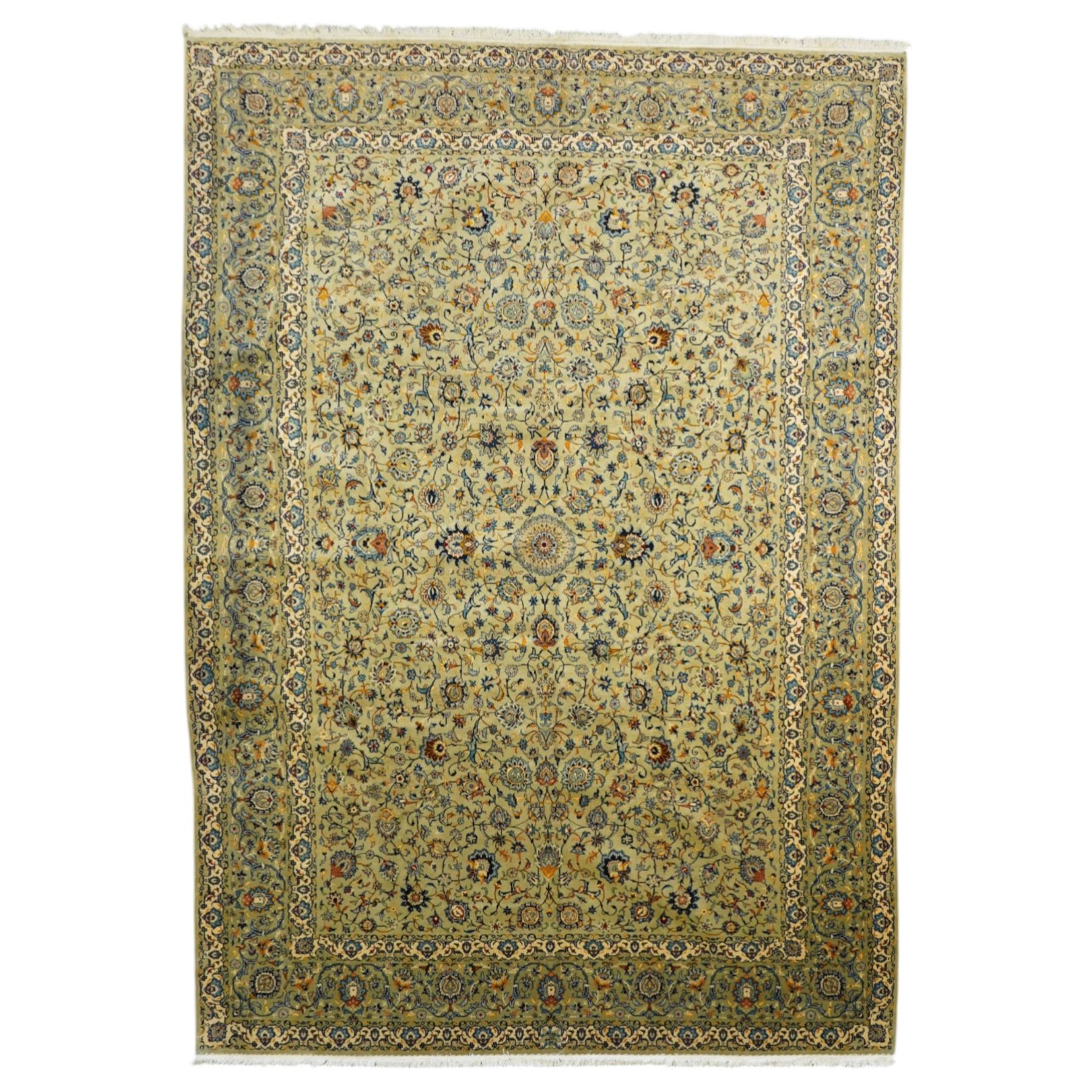 Central Persian Kashan hand-knotted carpet, pale blue field decorated with a finely drawn all-over scrolling floral vine design incorporating stylized palmettes, rosettes and foliate sprays, with a small central circular medallion, enclosed by a conforming floral vine border between multiple guard stripes, with cotton fringe ends  