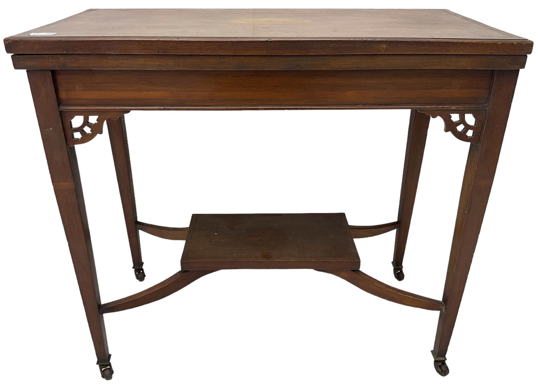 Edwardian inlaid mahogany games table, the rectangular fold-over swivel top decorated with central shell motif inlay and ebony stringing, raised on tapering supports united by shaped X-stretcher and undertier