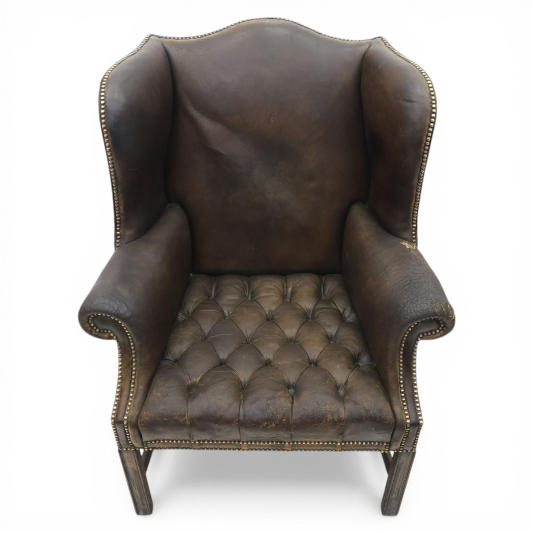Georgian style leather wing armchair, shaped high back with outscrolled wings above padded arms and deep buttoned seat, close-nailed throughout, raised on square supports united by H-stretcher