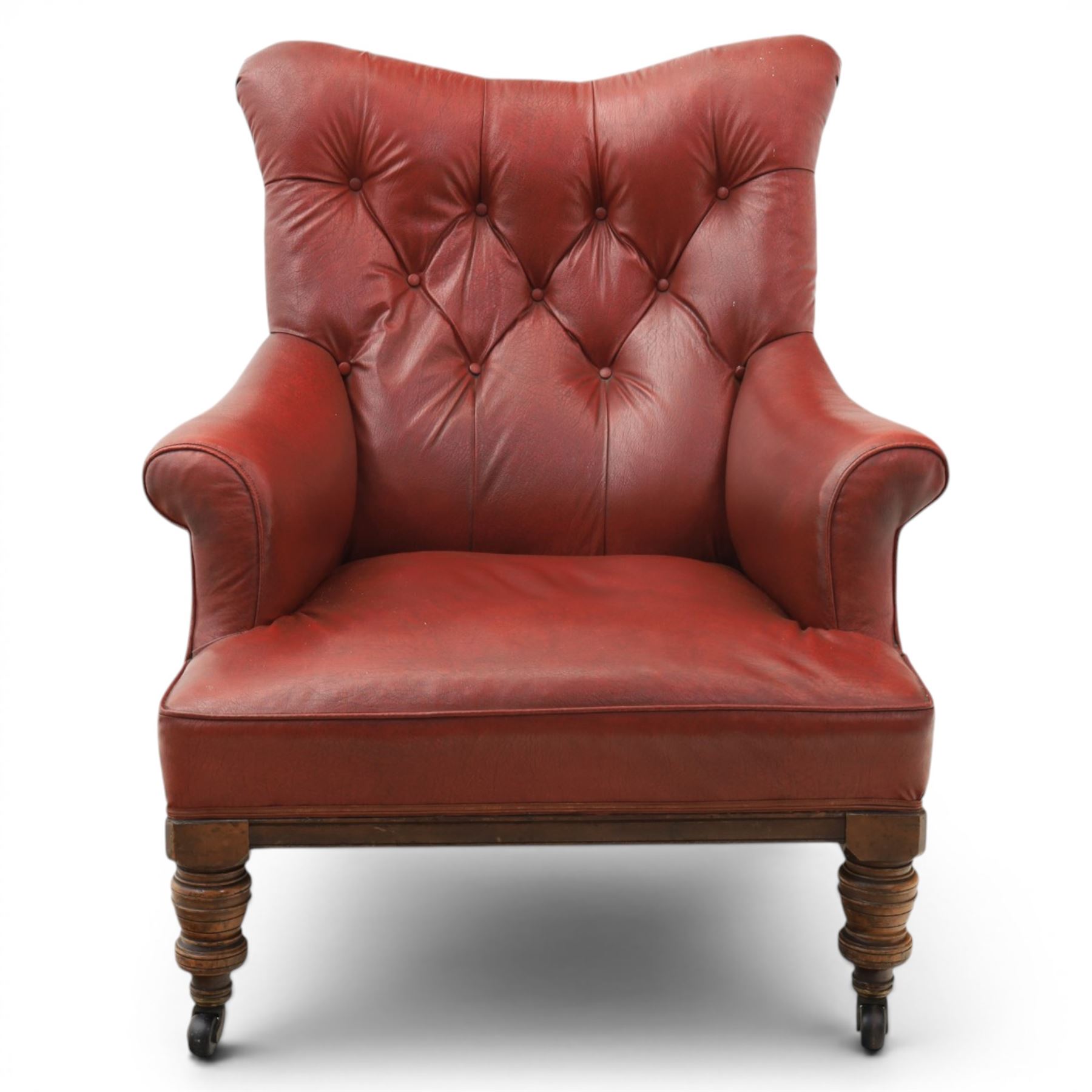 Early 20th century style oxblood red leather Chesterfield armchair, deep buttoned shaped back over padded scroll arms and loose seat cushion, raised on turned mahogany front supports with brass caps and castors