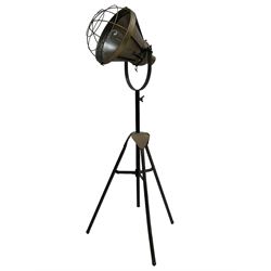 Industrial tripod spotlight, with a metal shade and wire guard, supported by a height-adjustable tripod base, the head equipped with an adjustable tilt mechanism