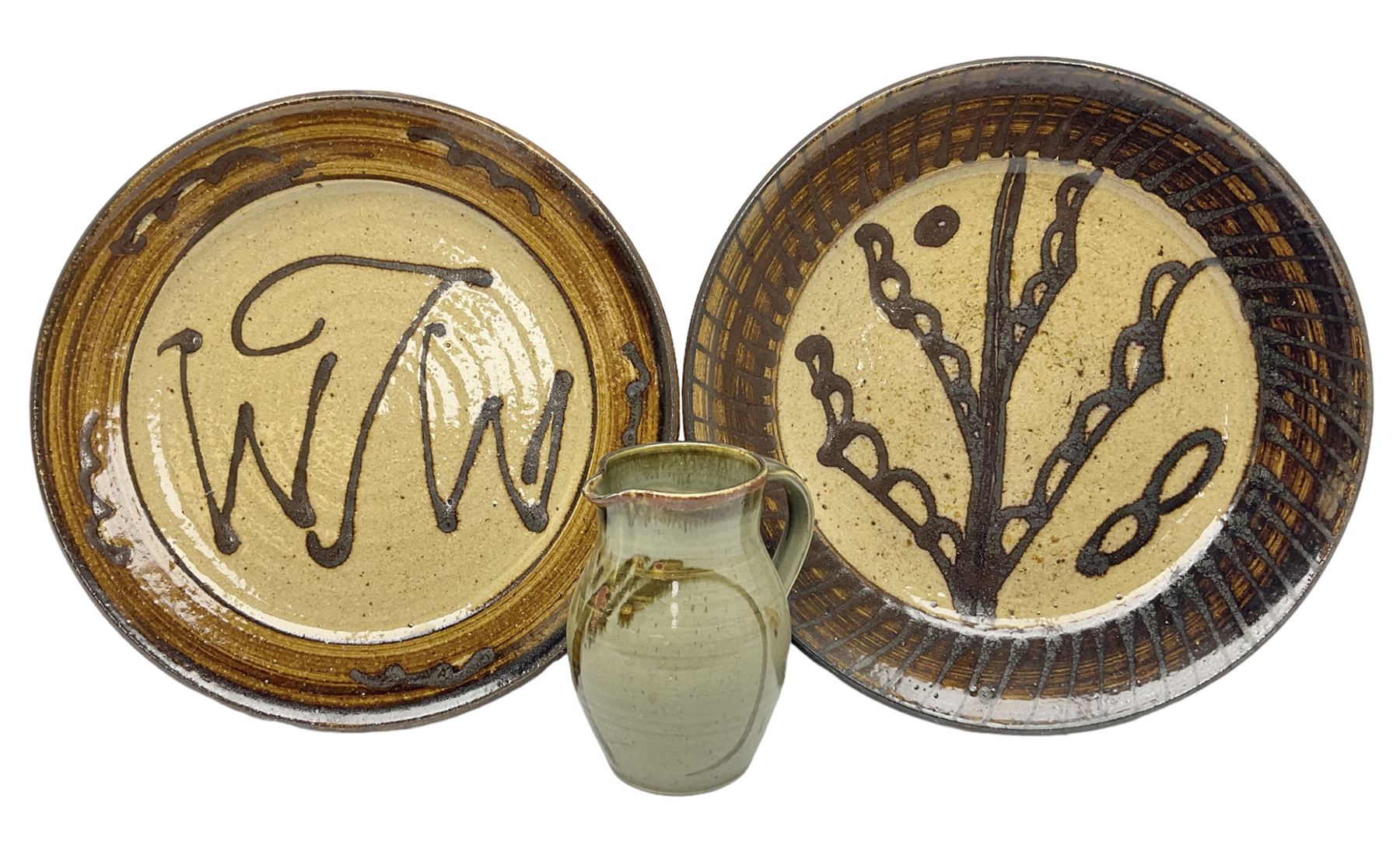 Michael Leach (British 1913-1985) for Yelland pottery; two large glazed stoneware plates with dark brown stylised decoration upon oatmeal ground, together with a jug in merging blue, green and brown, all with impressed marks beneath, largest plate D37cm