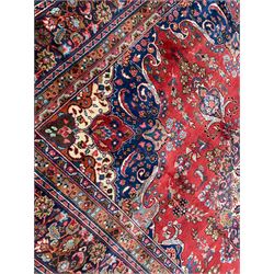 Persian Meshed crimson ground carpet, centre floral design medallion within a field of trailing branches and flower heads, scrolled spandrels decorated with flower heads, the main border decorated with stylised plant motifs within guard rails 