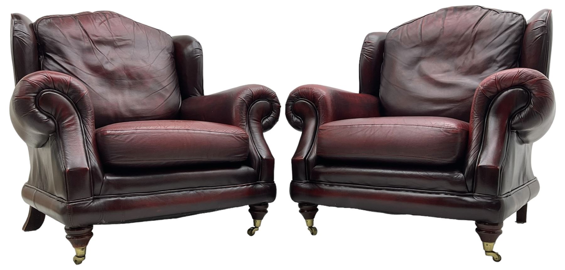 Thomas Lloyd - three-piece lounge suite, comprising of traditional shape two seat sofa (W190cm H80cm) and a pair of wingback armchairs (W100cm H91cm), each with rolled arms over turned supports with brass castors, upholstered in oxblood red leather